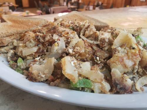 A plate of savory hash made with potatoes, onions, and green peppers, served with slices of toasted bread.