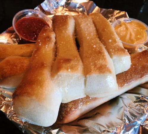 A plate of golden-brown breadsticks served with marinara and cheese dipping sauces.