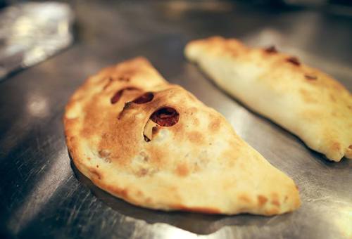 Two golden-brown calzones with visible fillings, resting on a shiny metal surface.