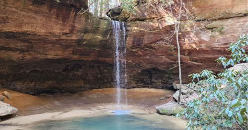 A serene waterfall cascades into a tranquil pool, surrounded by rocky cliffs and lush greenery.