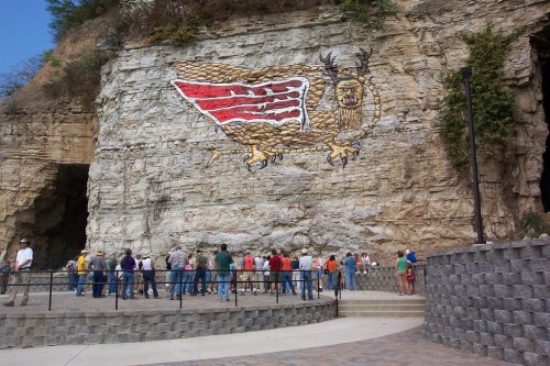 A large mural of a mythical creature on a rocky cliff, with a crowd of people gathered below.