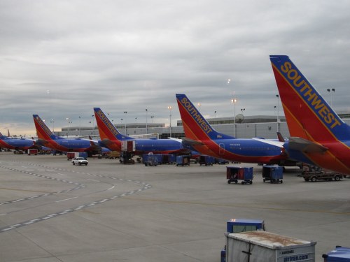 Southwest Airlines planes lined up at an airport terminal under a cloudy sky.