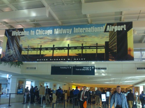 Banner welcoming visitors to Chicago Midway International Airport, featuring a sunset skyline and crowds in the terminal.