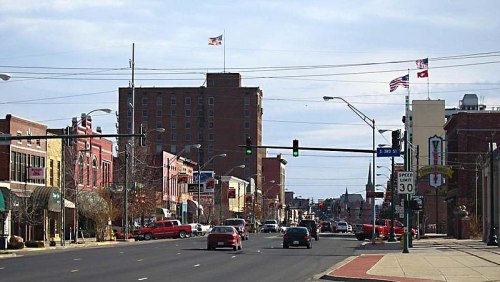 A busy street scene with shops, traffic lights, and flags flying above buildings in a small town.
