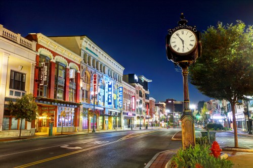 A quiet street at night featuring a vintage clock and colorful storefronts illuminated by city lights.