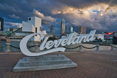 Cleveland sign in foreground with city skyline and dramatic clouds in the background.