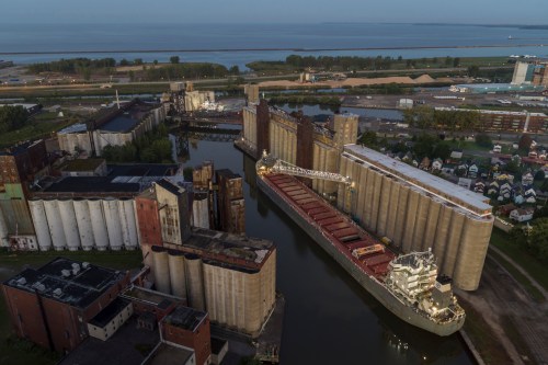 Aerial view of a port with grain silos, a cargo ship, and a calm waterway at dawn.