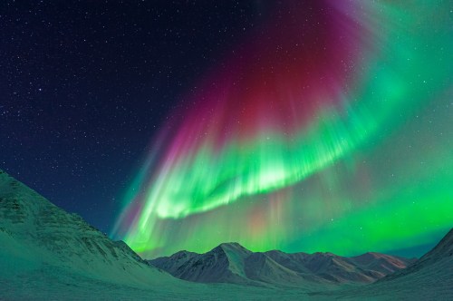 Vibrant aurora borealis lights up the night sky over snow-covered mountains.
