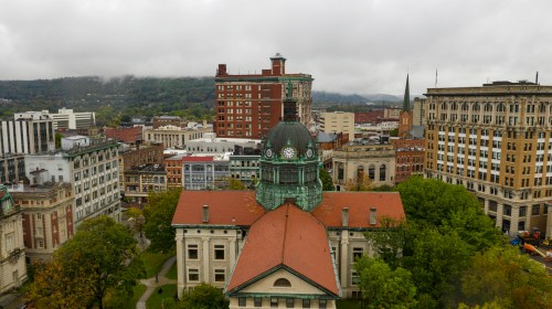 Aerial view of a cityscape featuring historic buildings, a clock tower, and overcast skies with mountains in the background.
