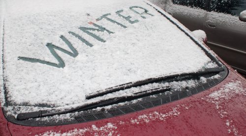 A car windshield covered in snow with the word "WINTER" written in the snow.