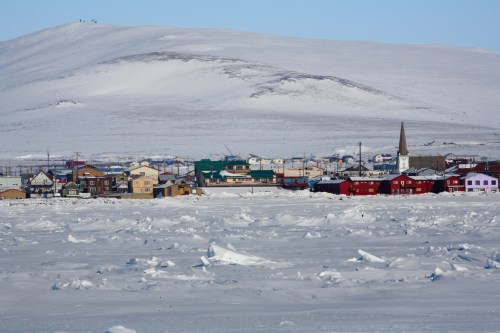 A snowy landscape with a small town featuring colorful buildings and a church, set against a backdrop of mountains.