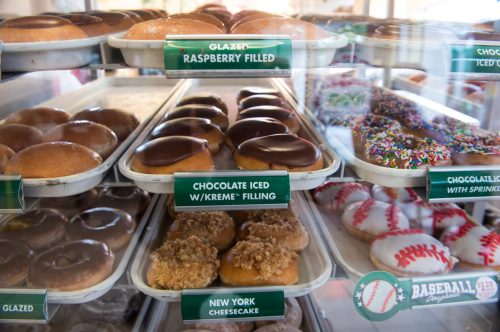 A display case filled with various donuts, including glazed, raspberry filled, chocolate iced, and New York cheesecake.