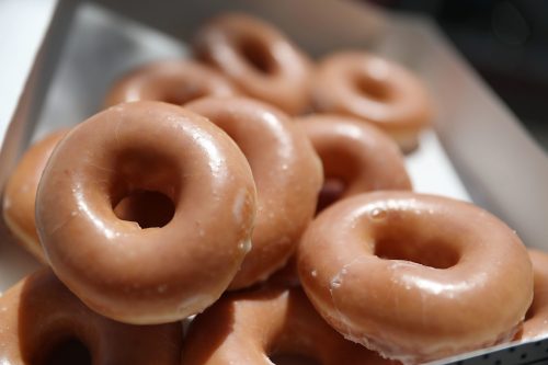 A close-up of glazed donuts stacked in a box, showcasing their shiny, golden-brown surface.