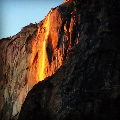 A stunning view of a waterfall cascading down a rocky cliff, illuminated by golden sunlight at sunset.