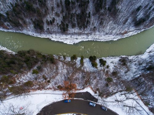 Aerial view of a winding river surrounded by snowy trees and a curved road at the edge of a forested area.