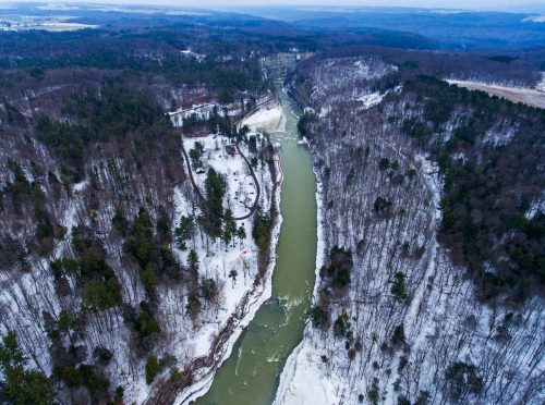 Aerial view of a winding river surrounded by snow-covered trees and hills in a winter landscape.