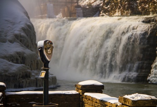 A frozen waterfall cascades in the background, with a parking meter in the foreground on a snowy day.
