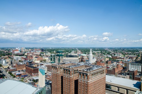 Aerial view of a city skyline with buildings, streets, and a clear blue sky dotted with clouds.