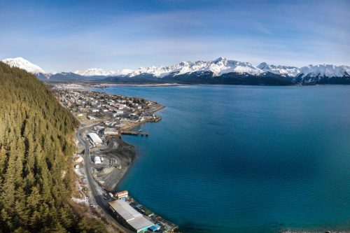 Aerial view of a coastal town surrounded by mountains and a calm blue sea under a clear sky.