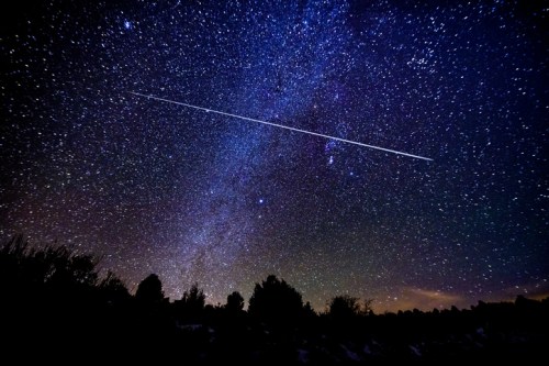 A starry night sky filled with stars and a bright meteor streaking across the scene.