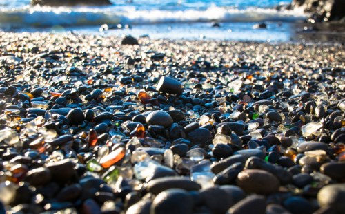 Colorful sea glass and smooth stones scattered on a beach, with gentle waves in the background.
