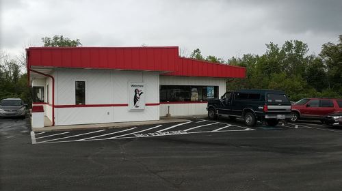A small building with a red roof and a "Welcome" sign, surrounded by parked cars and greenery.