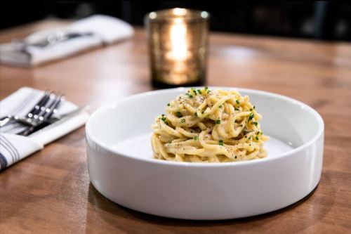 A plate of creamy pasta topped with chives, set on a wooden table with a candle in the background.
