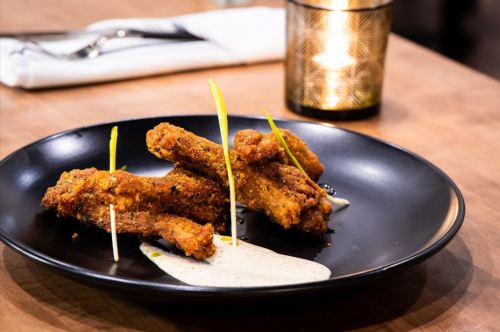 Crispy fried chicken wings on a black plate, garnished with green skewers and served with a creamy dipping sauce.