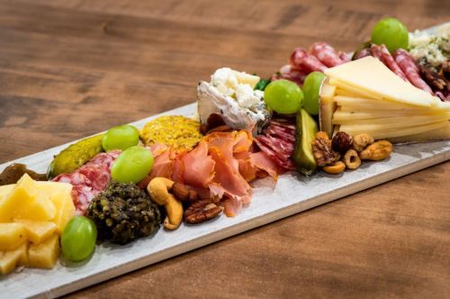 A charcuterie board featuring various cheeses, meats, nuts, grapes, and condiments on a wooden surface.