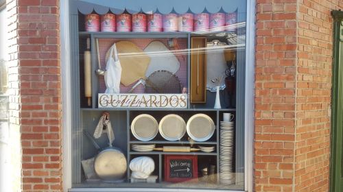 A storefront window display featuring baking tools, plates, and a sign that says "Welcome" with a red door motif.