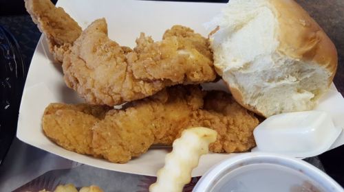 A plate with three crispy chicken tenders, a soft bread roll, a dipping sauce, and a side of crinkle-cut fries.
