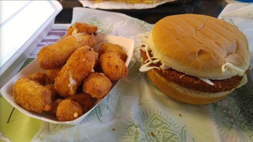 A crispy chicken sandwich with lettuce next to a serving of golden, breaded cheese bites on a tray.