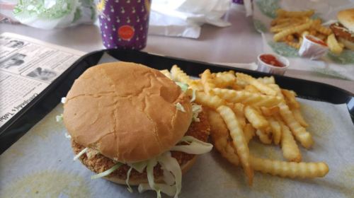 A crispy chicken sandwich with lettuce, served with a side of crinkle-cut fries and dipping sauce on a tray.