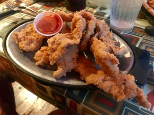 A sizzling platter of golden fried chicken tenders served with a small cup of dipping sauce.