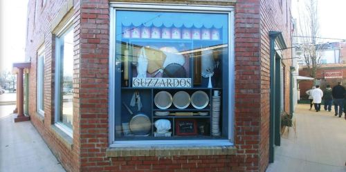 A storefront window displays various kitchen items and utensils, with the name "Guzzardo's" prominently featured.