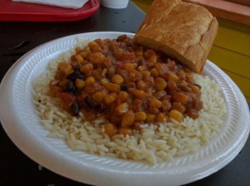 A plate of rice topped with a bean and corn mixture, accompanied by a piece of bread.