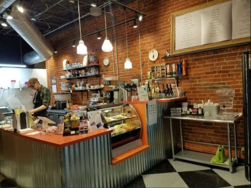 A cozy café interior with a brick wall, counter displaying pastries, and a barista preparing drinks.
