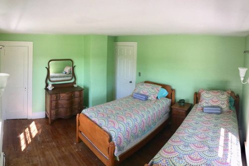 A bright green bedroom with two wooden beds, colorful bedding, a dresser, and a mirror reflecting the room.