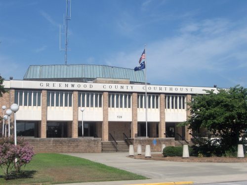 Exterior view of the Greenwood County Courthouse, featuring a flag, modern architecture, and landscaped surroundings.