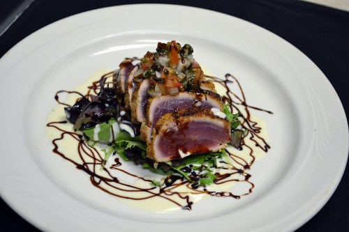 A plate of seared tuna slices on a bed of greens, topped with salsa and drizzled with balsamic reduction.