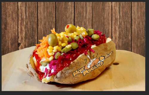 A loaded baked potato topped with colorful vegetables, corn, and sauces, served on a wooden surface.