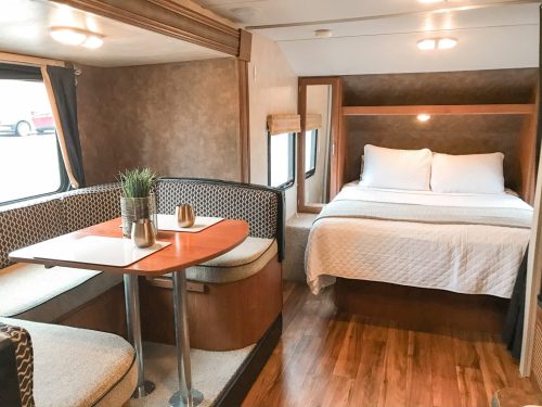 Cozy interior of a camper with a dining area and a double bed, featuring warm lighting and wooden flooring.