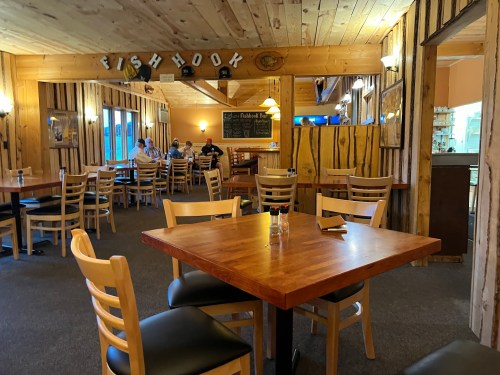 Cozy restaurant interior with wooden decor, empty tables, and patrons in the background enjoying their meals.