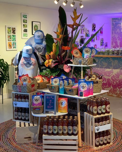 A vibrant display of colorful products, including drinks and apparel, surrounded by tropical plants in a shop setting.