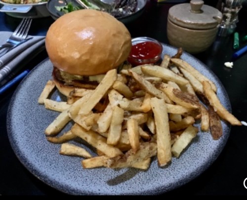 A plate with a burger and a generous serving of golden fries, accompanied by a small dish of ketchup.