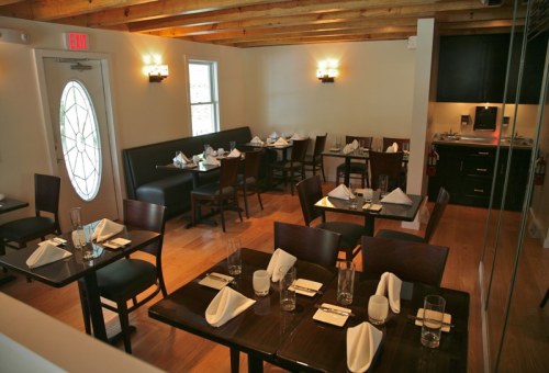 A cozy restaurant interior with wooden beams, tables set for dining, and a welcoming entrance.