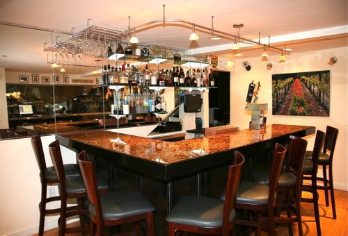 A stylish bar with a polished countertop, high stools, and shelves stocked with various bottles and glasses.