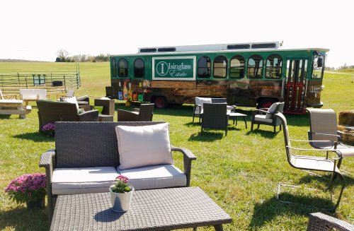 A cozy outdoor seating area with a vintage trolley in the background, surrounded by green fields and flowers.