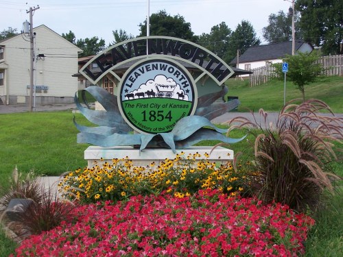 Sign welcoming visitors to Leavenworth, Kansas, established in 1854, surrounded by colorful flowers and greenery.