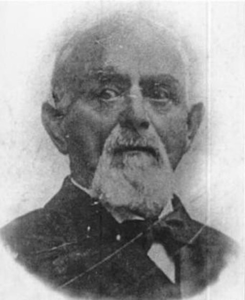 Black and white portrait of an elderly man with a mustache and beard, wearing a suit and bow tie.